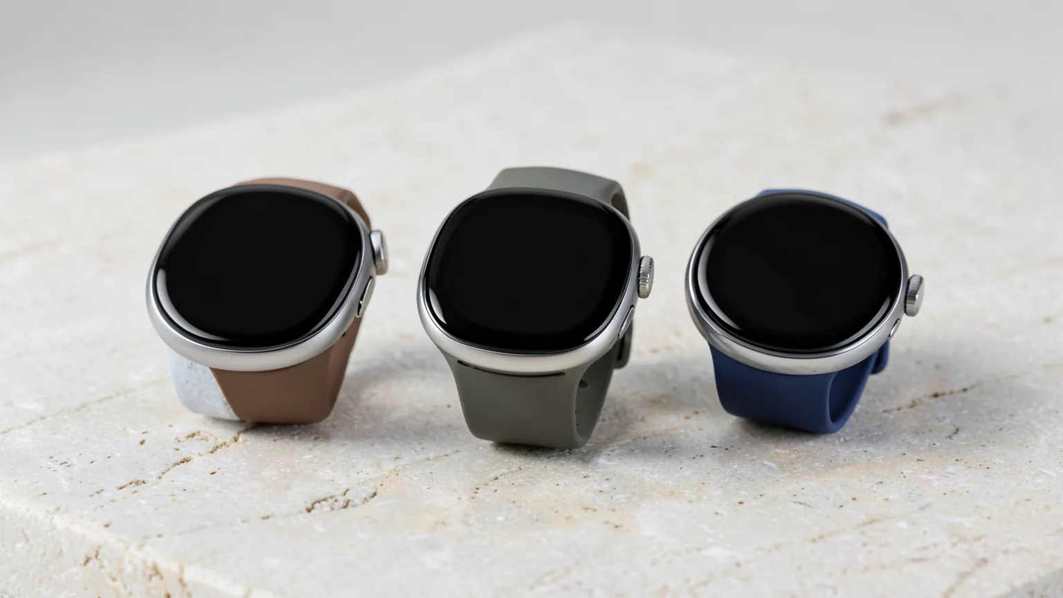 Tres relojes inteligentes de distintos tamanos y acabados colocados sobre una superficie de piedra clara