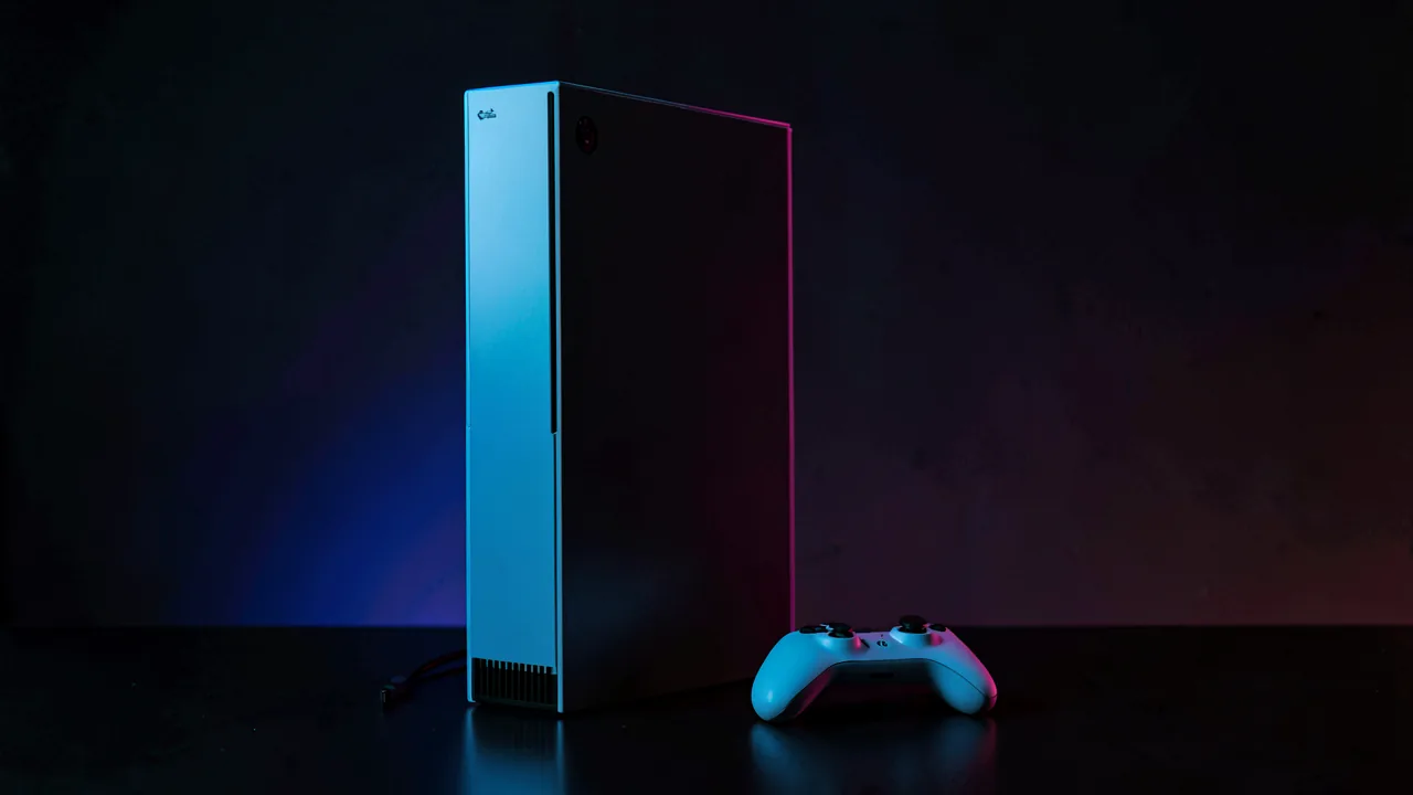 Consola PlayStation 5 en vertical junto a un mando inalámbrico blanco con iluminación azul y magenta