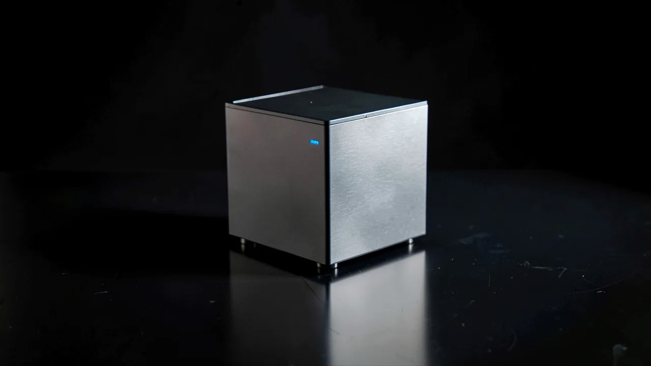 Mini PC de aluminio compacto con indicador LED azul sobre una superficie oscura reflectante