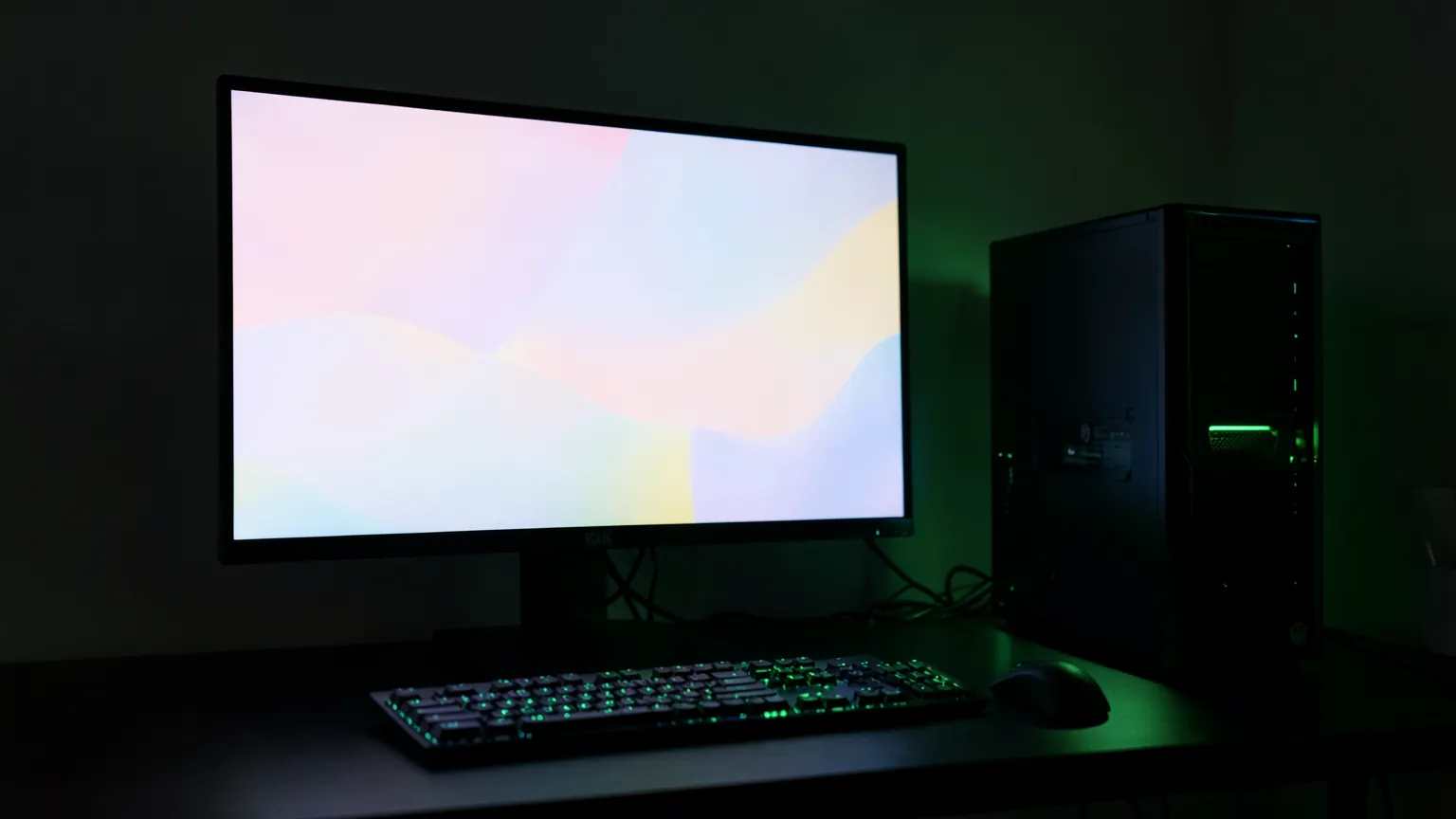 Escritorio con un monitor grande de colores suaves abstractos junto a un PC con iluminación verde